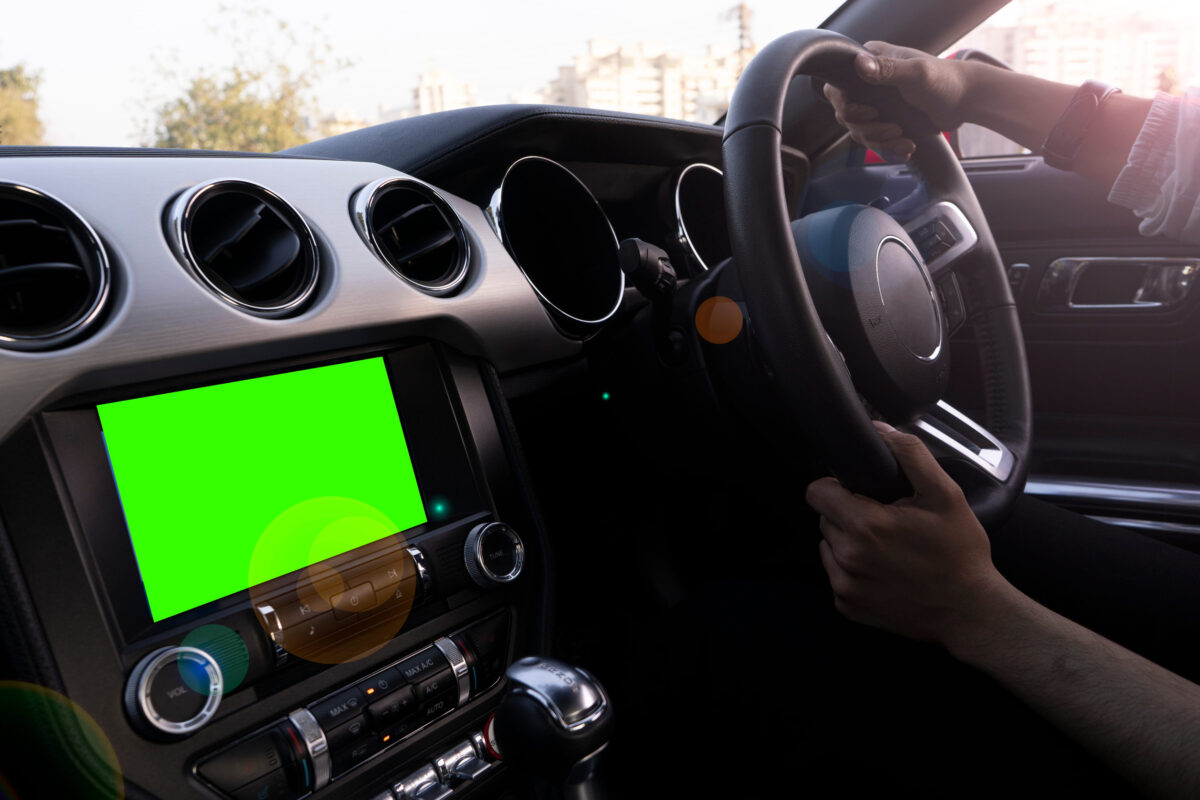 Interior of a luxury car with black leather finish, with a green screen on the dashboard. Man driving the car.
