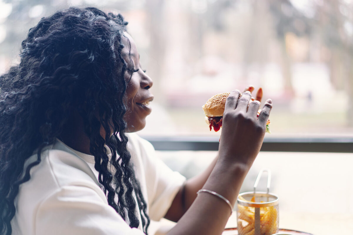 African woman with afro hair eating a tasty classic burger with fries.
