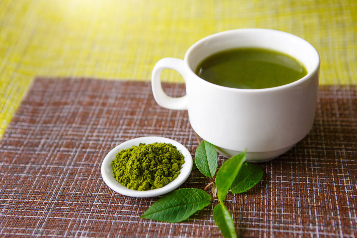 Japanese matcha green tea is poured into a white mug and on a white saucer in powder. Tea set on a textured napkin of natural flowers, decorated with a branch of green leaves. Cup with mock up
