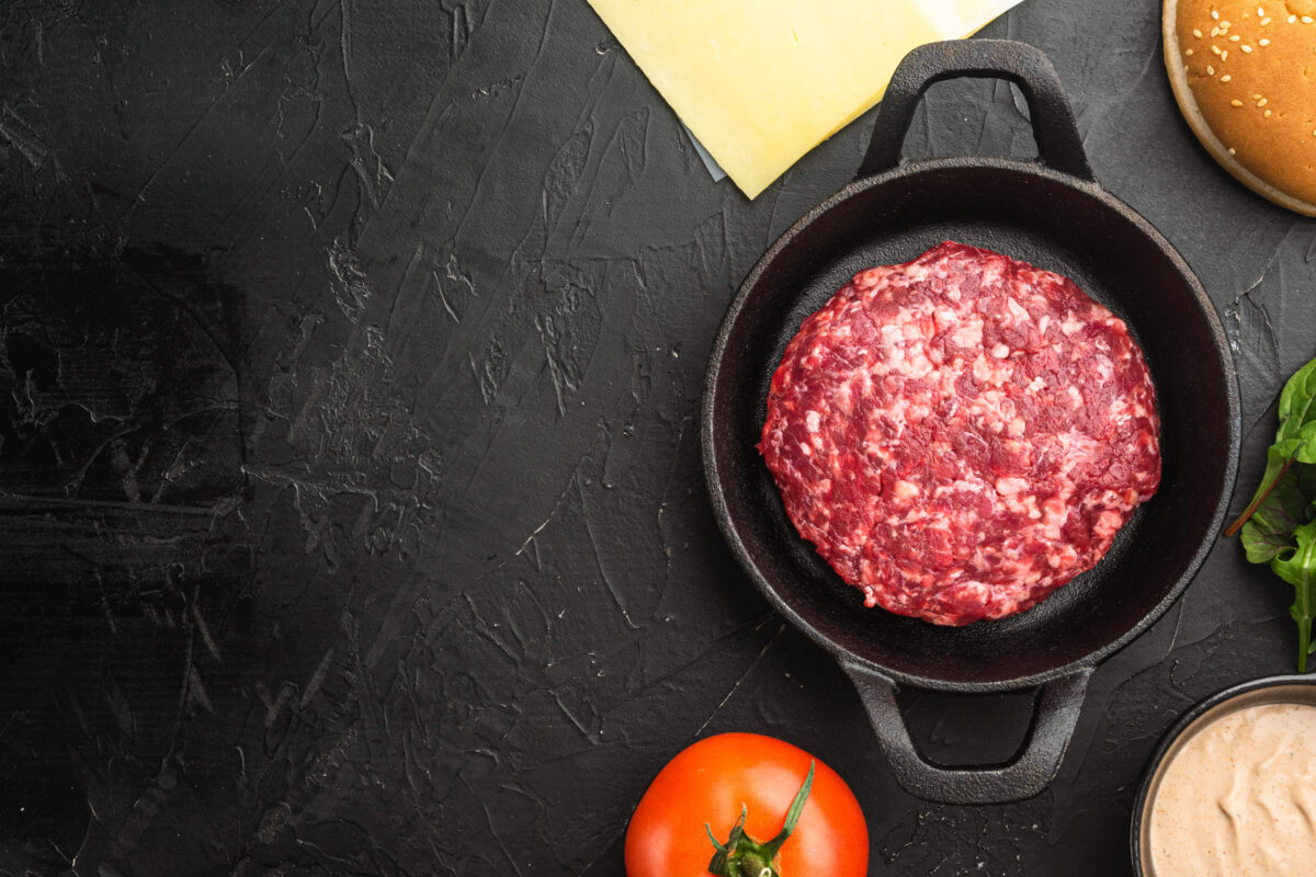 Homemade hamburger. Raw beef patties, sesame buns with other ingredients set, on black stone background, top view flat lay, with copy space for text