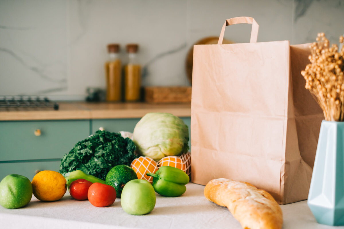 7 Kitchen Habits That Make Food Spoil Faster Than It Should 1 Eco shopping paper bag with fresh vegetables and baguette on the table in modern kitchen. Food delivery or market shopping concept.