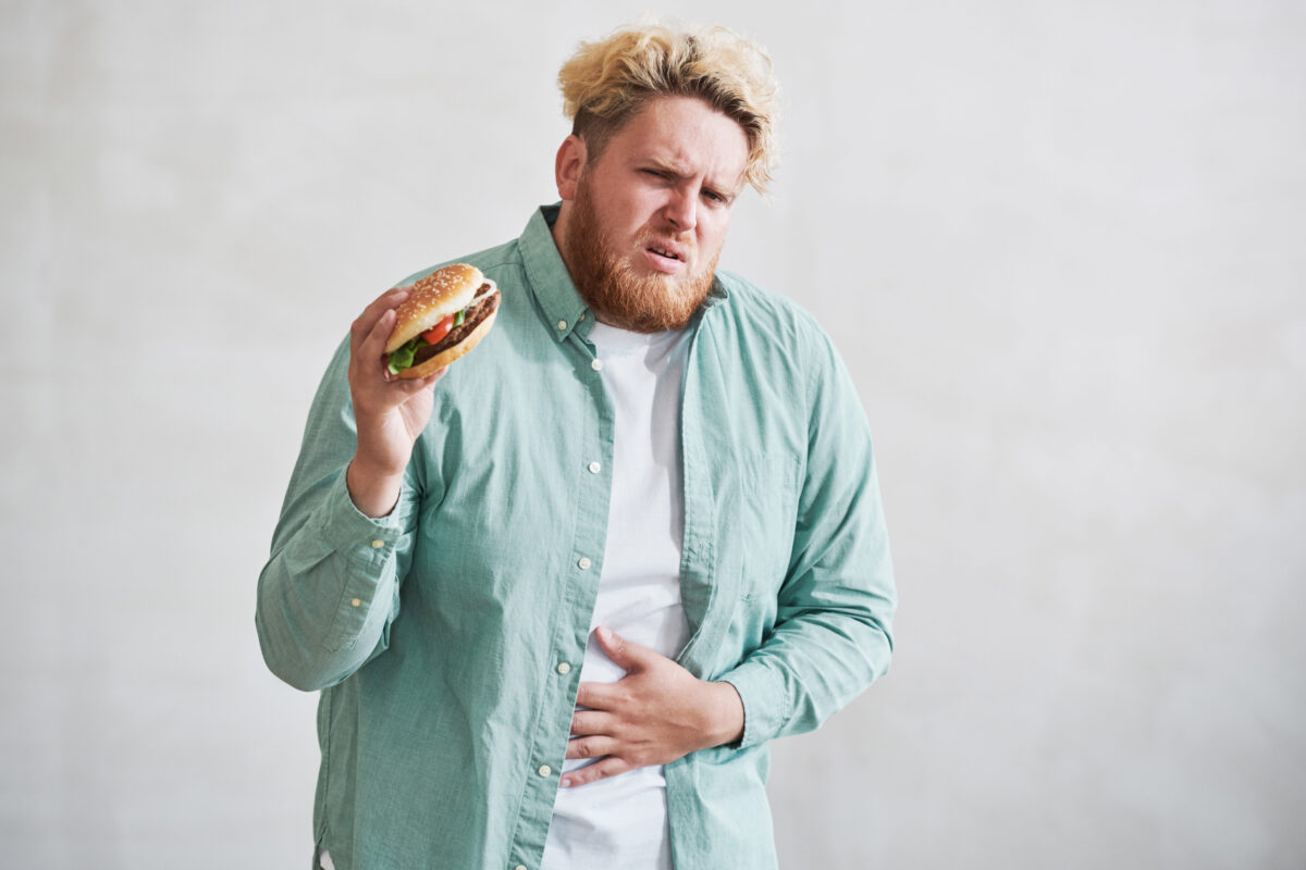 Overweight man having a stomach ache from eating of fast food against the white background