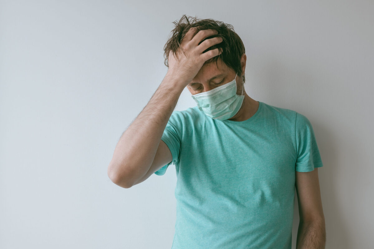 Man with mask having migraine headache as Covid-19 symptoms, portrait of male person with virus infection during pandemics