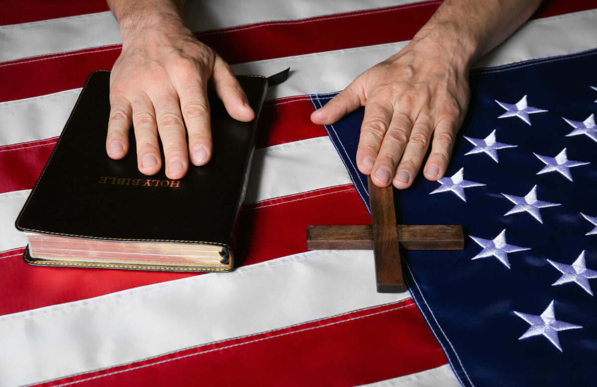 Man with Holy Bible and cross on USA flag, closeup