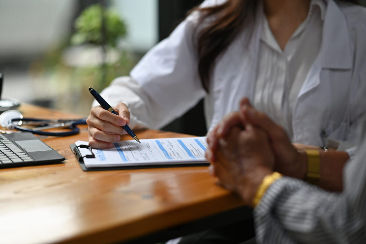 Cropped image of a beautiful doctor diagnosing and giving advice to the elderly patient at the working desk over a comfortable hospital as background.