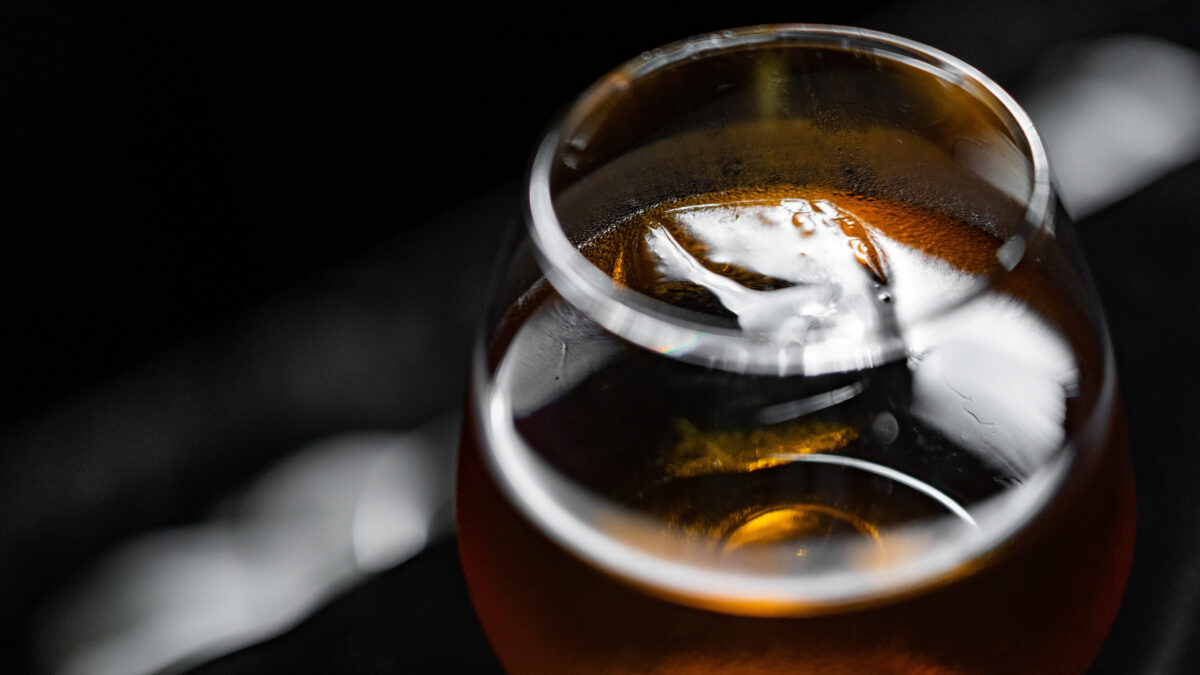 A glass of brandy with ice cubes on a black background