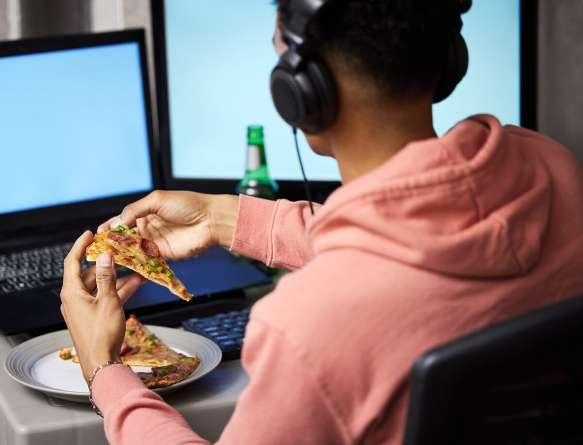 Pizza is a must during game night. Rearview shot of a young man eating pizza while playing video games at home.