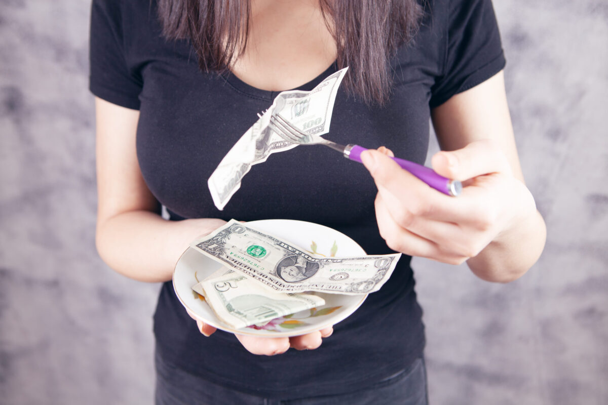 young girl with a fork eats money on a gray background