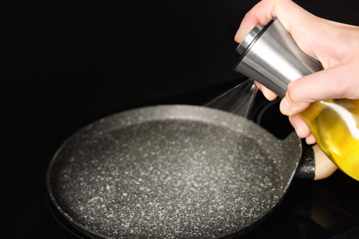 Woman spraying cooking oil onto frying pan on stove, 
