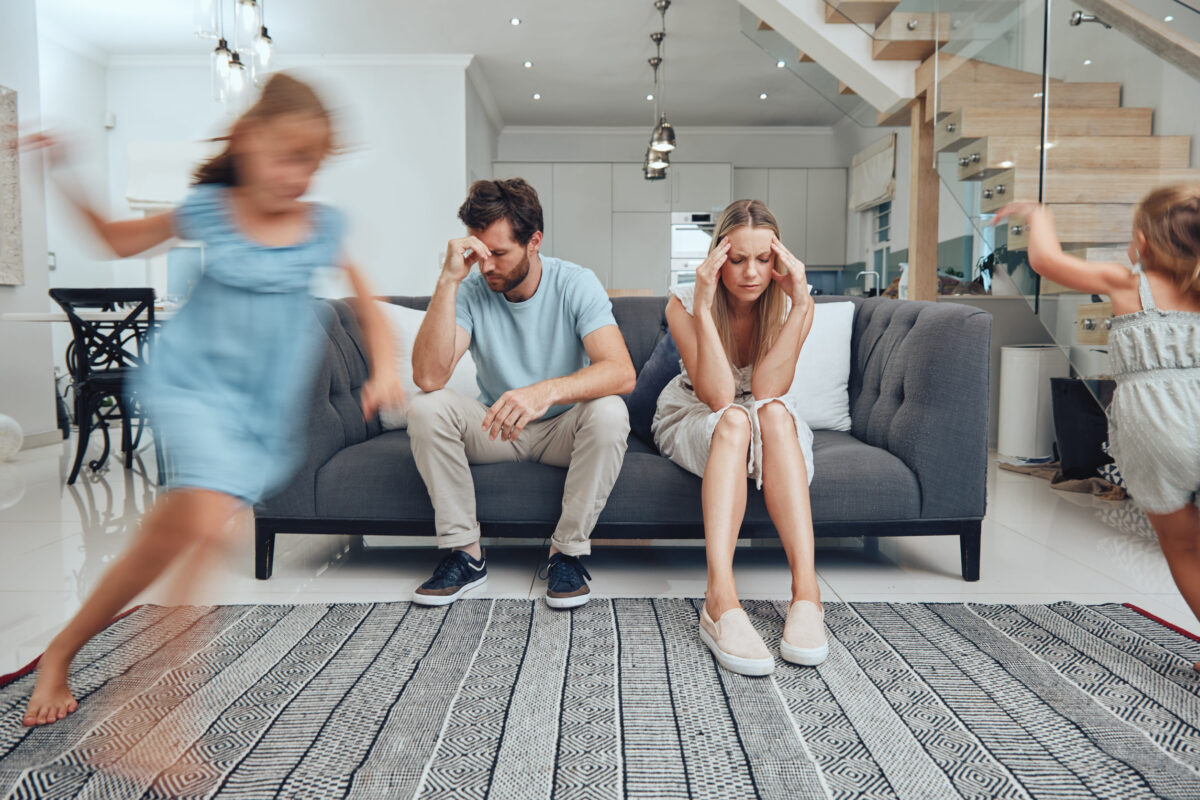 Tired parents, child energy and parent care burnout with anxiety from adhd children at home. Headache, stress and noise from girl kids in a living room busy with mom and dad on a sofa with fatigue