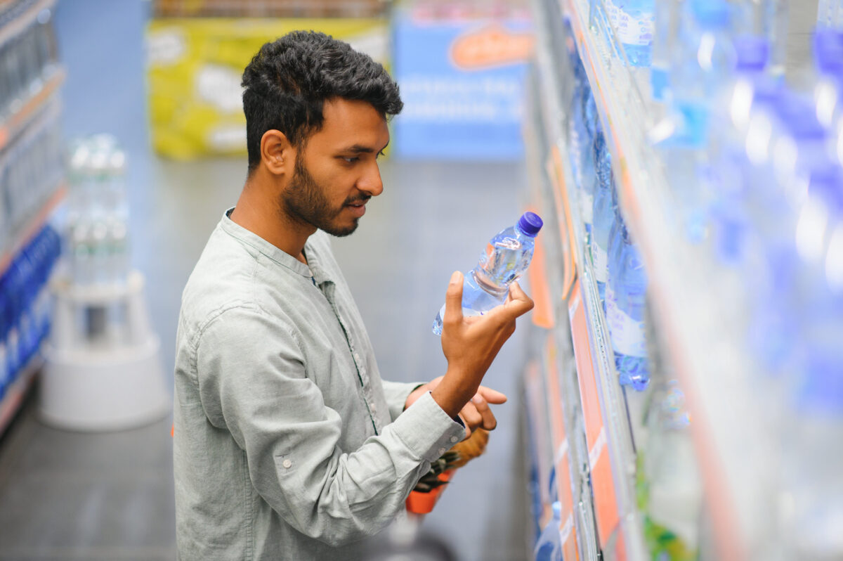 Portrait of happy Indian man standing in front of the product counter in a grocery store. Man buying groceries for home in supermarket