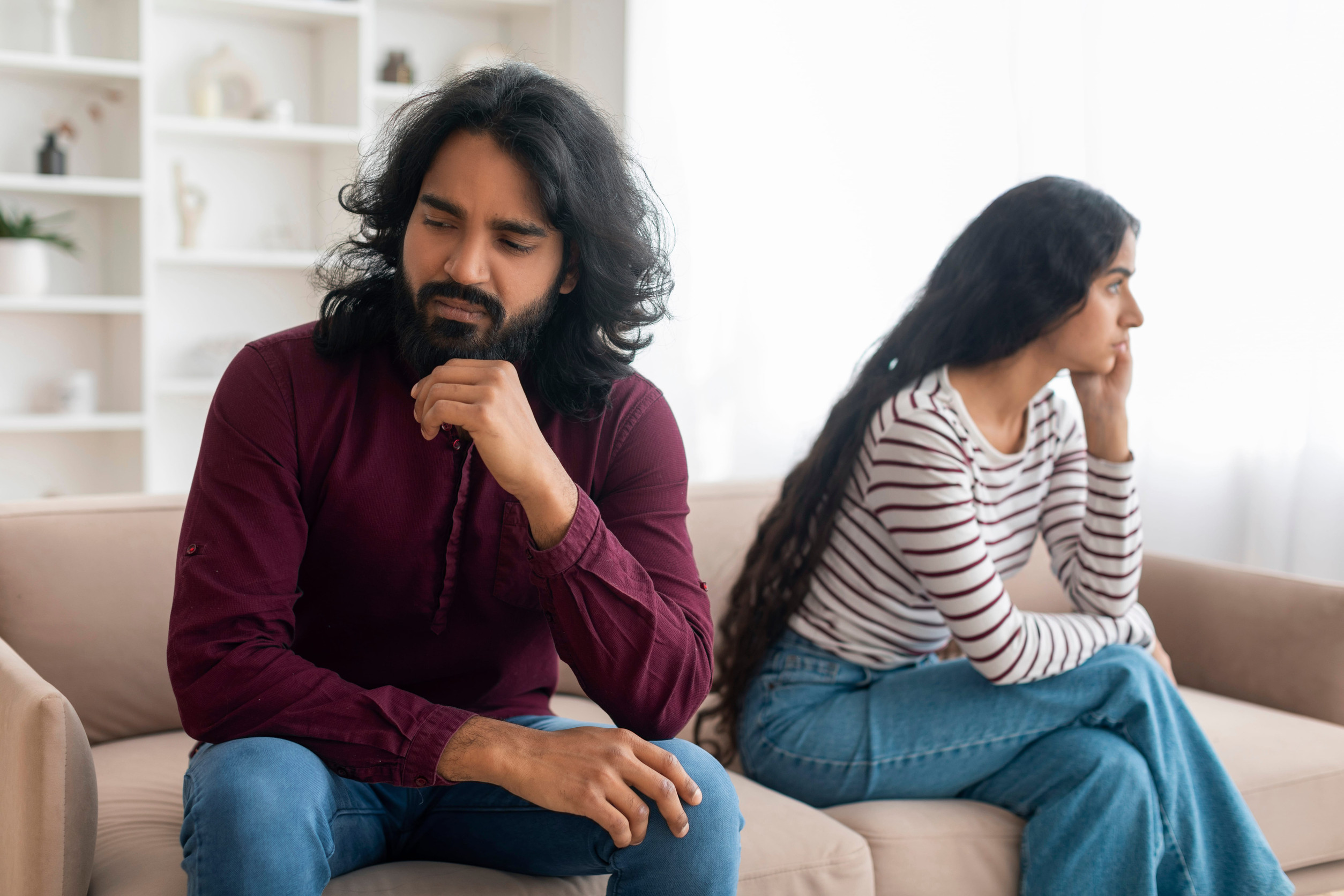 unhappy young couple sitting on couch far from each other
