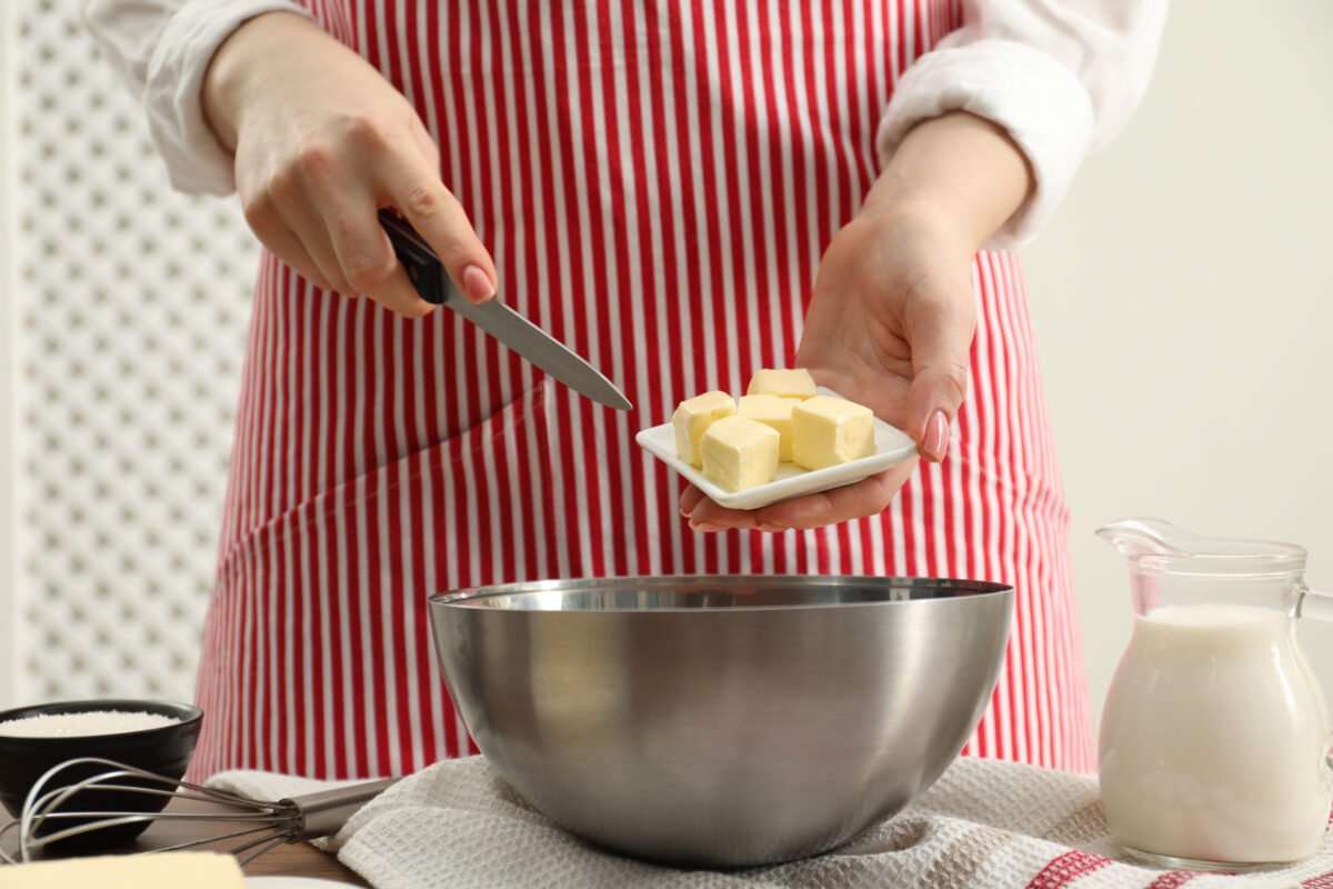 Woman adding fresh butter into bowl at table, closeup