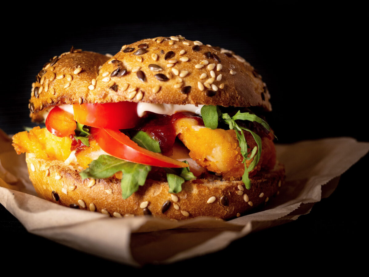 Fresh, delicious burgers with a beef patty, lettuce, onions, tomatoes and cucumbers. A large, fresh hamburger with overflowing cheese filling. On a wooden table isolated on a dark background.