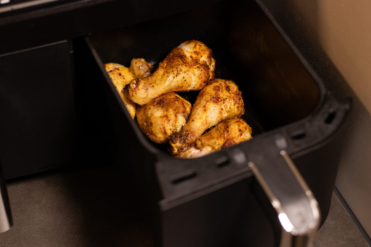 Close up an open air fryer with roasted chicken drumsticks inside