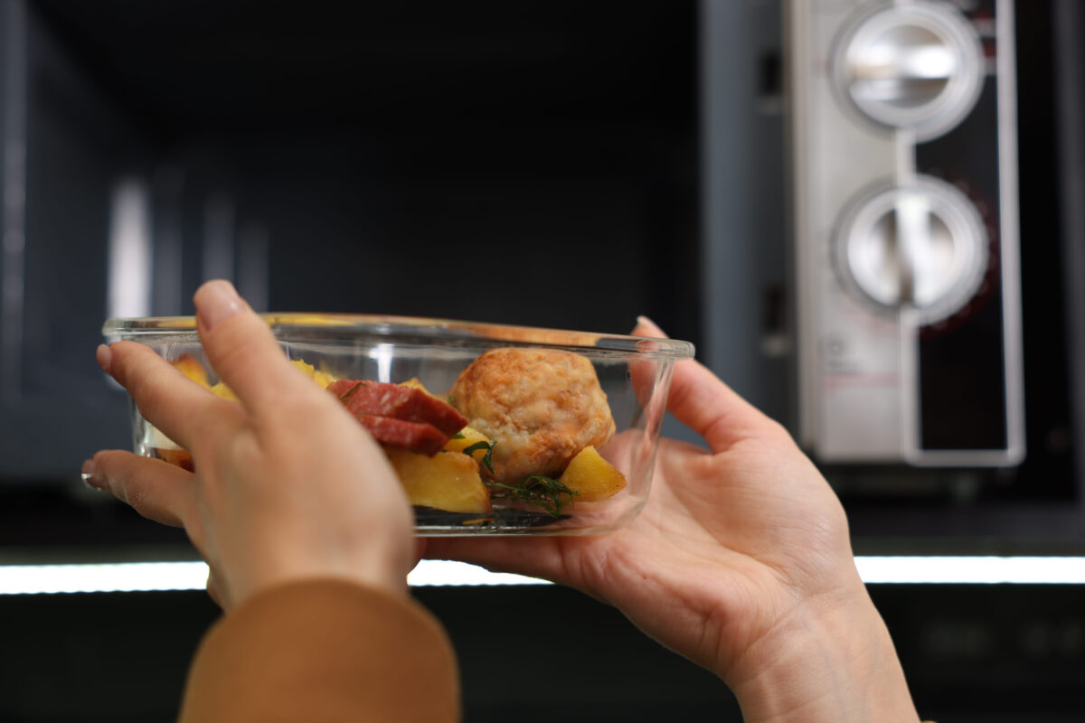 Woman putting container with lunch into microwave indoors, closeup