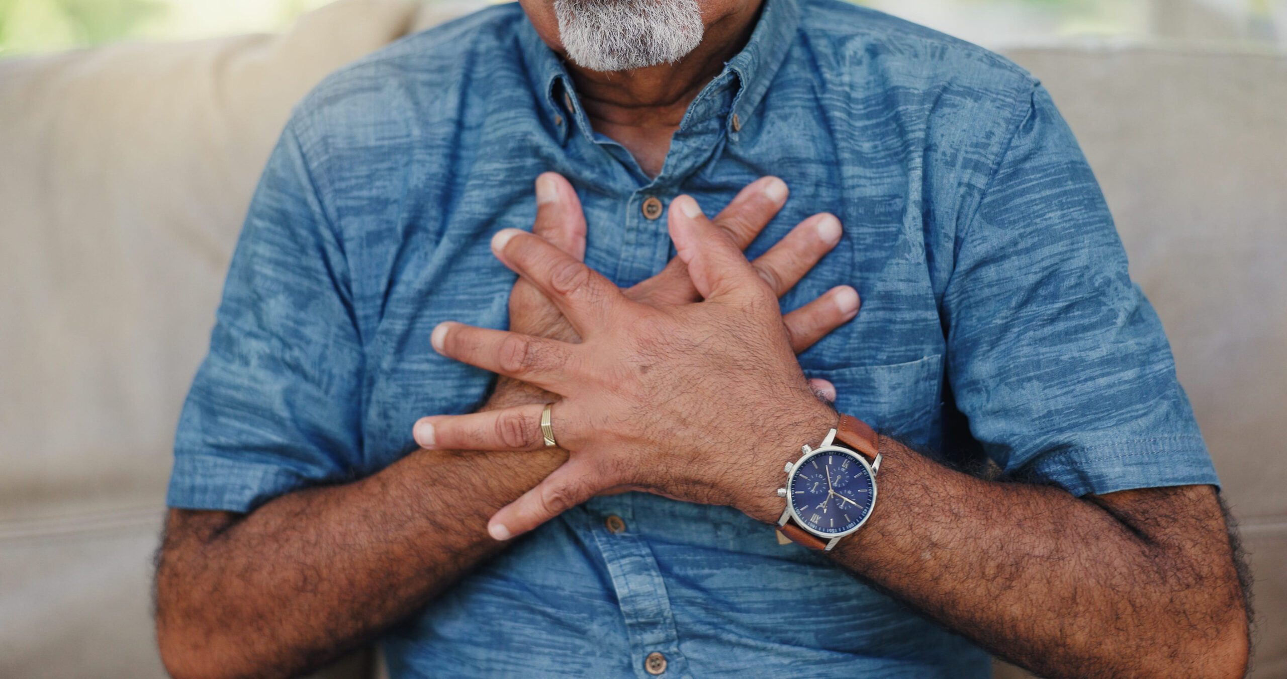 Senior man, hands and chest pain with heart attack on sofa for hypertension, artery pressure or medical emergency. Cardiovascular, elderly person or discomfort with breathing or health crisis in home