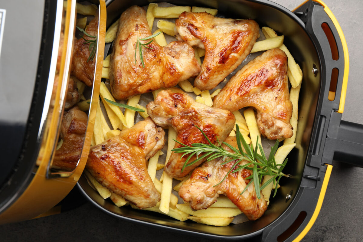 Grilled chicken wings, French fries and rosemary in air fryer on gray table, top view