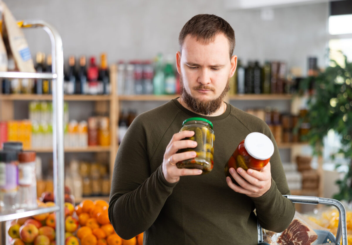 Man carefully selects canned tomatoes and cucumbers in the 