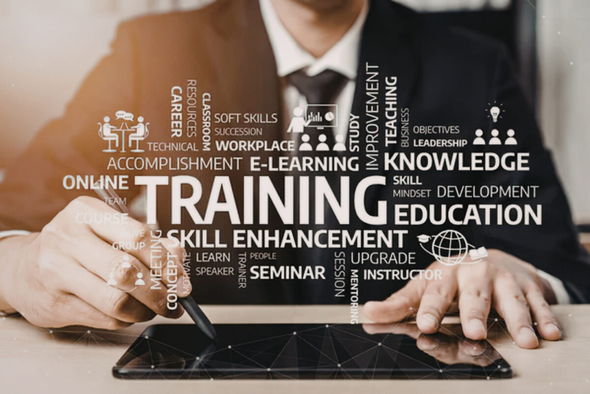 Professional man in suit using stylus on digital tablet surrounded by related training keywords and icons representing online education and skill development concepts.