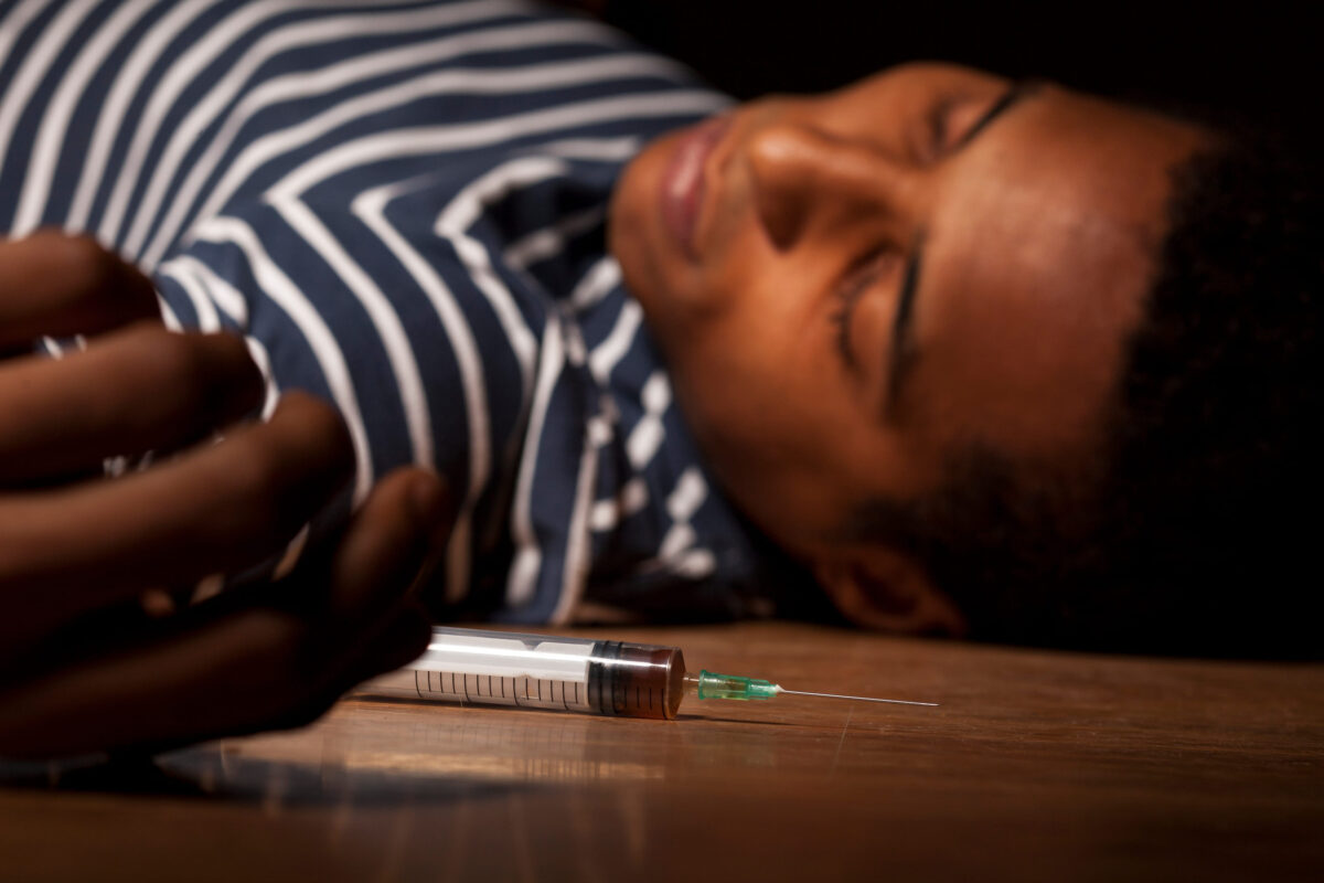 Young dark-skinned man lying on the floor with a syringe in his hand