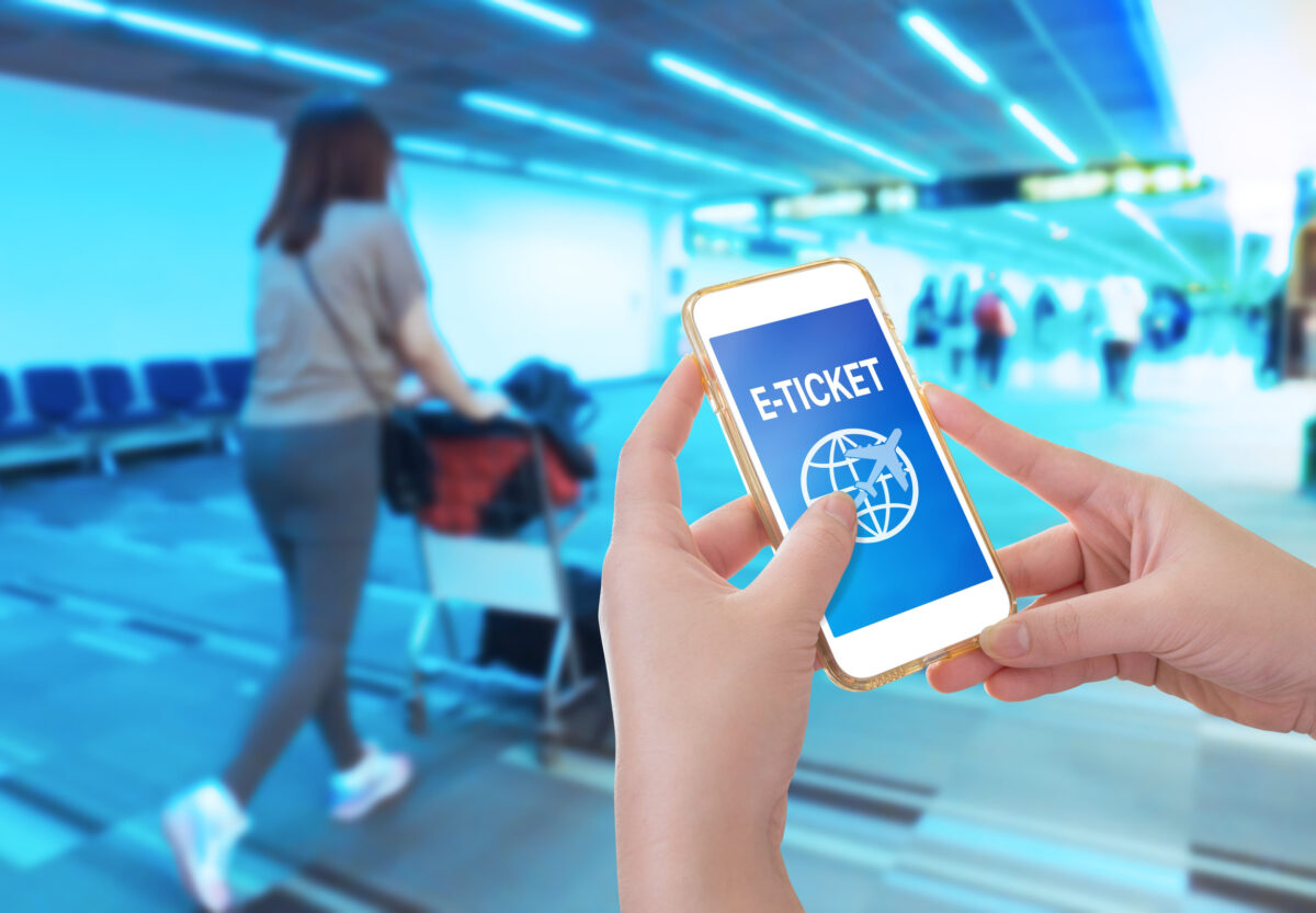 Hand holding mobile phone with Blurred image of passenger pushing luggage cart in airport terminal