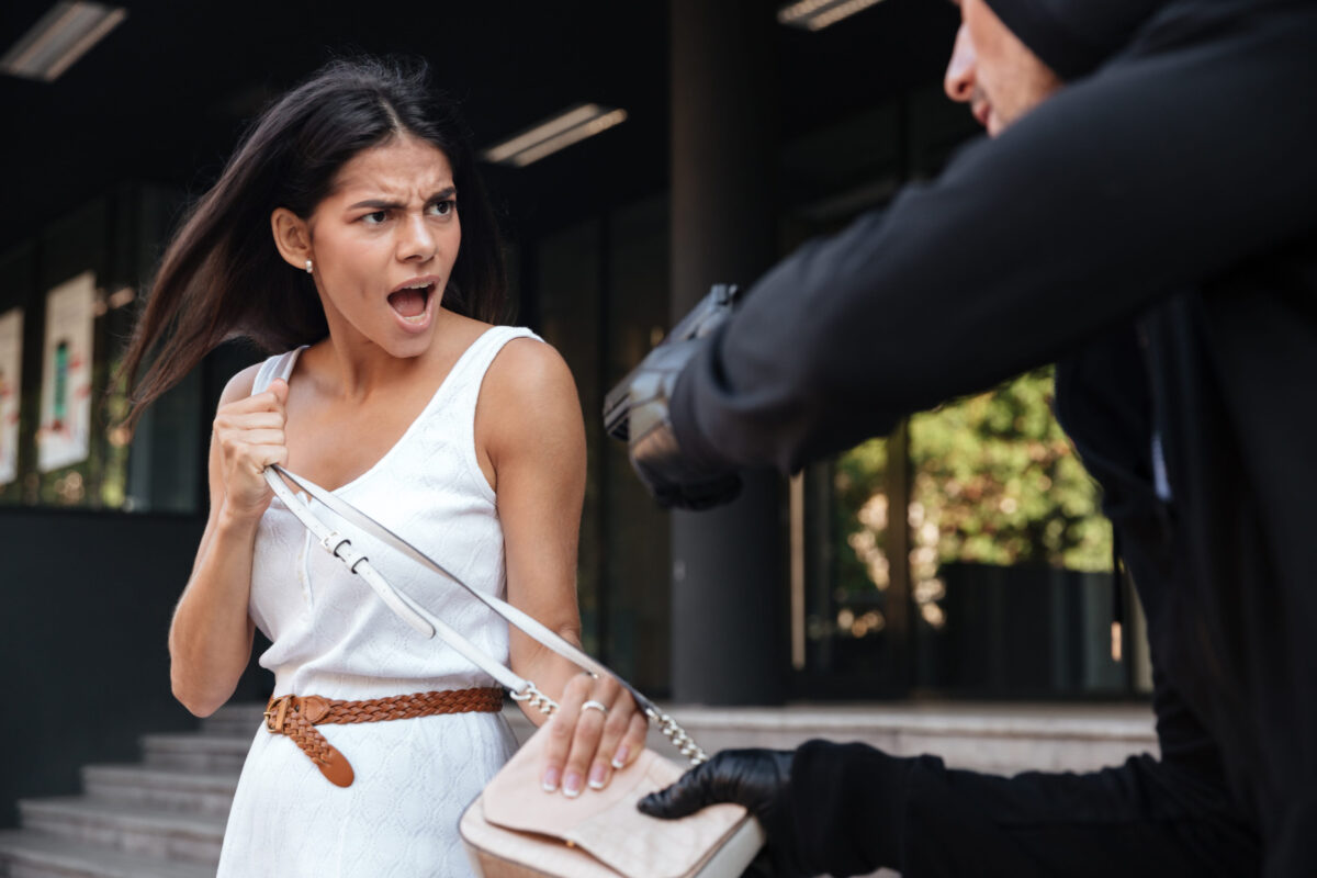 Angry young woman shouting and protecting from man thief with gun on the street