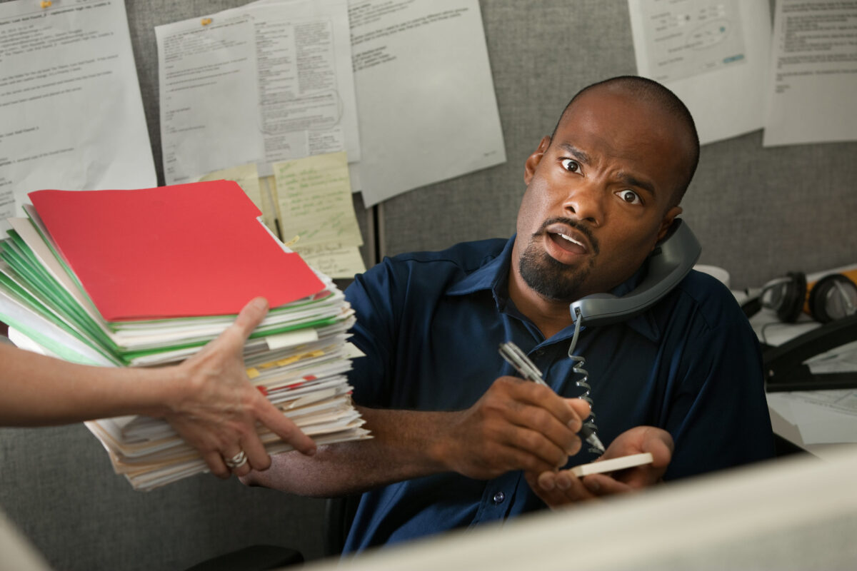Shocked African-American office worker on a phone call given a stack of files
