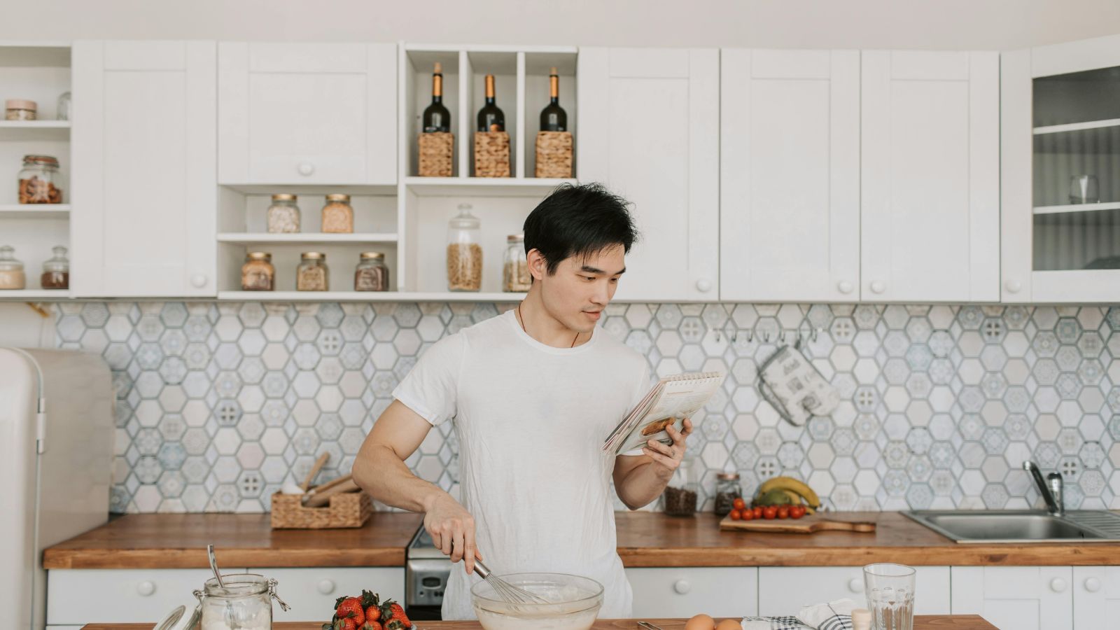 Young Asian man preparing a meal in a stylish kitchen reading a recipe while mixing ingredients