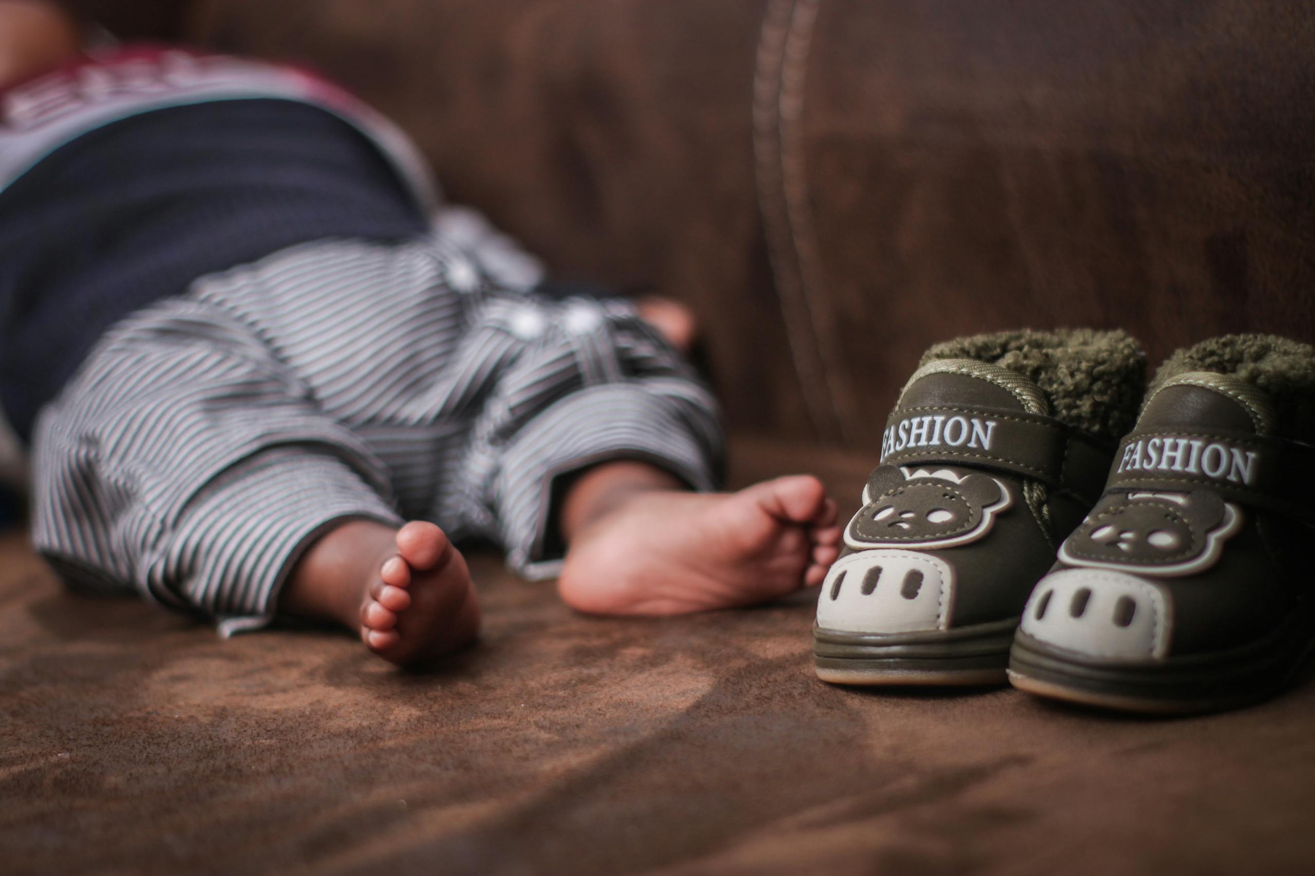 A baby's feet lie next to cute animal-themed shoes on a cozy couch.