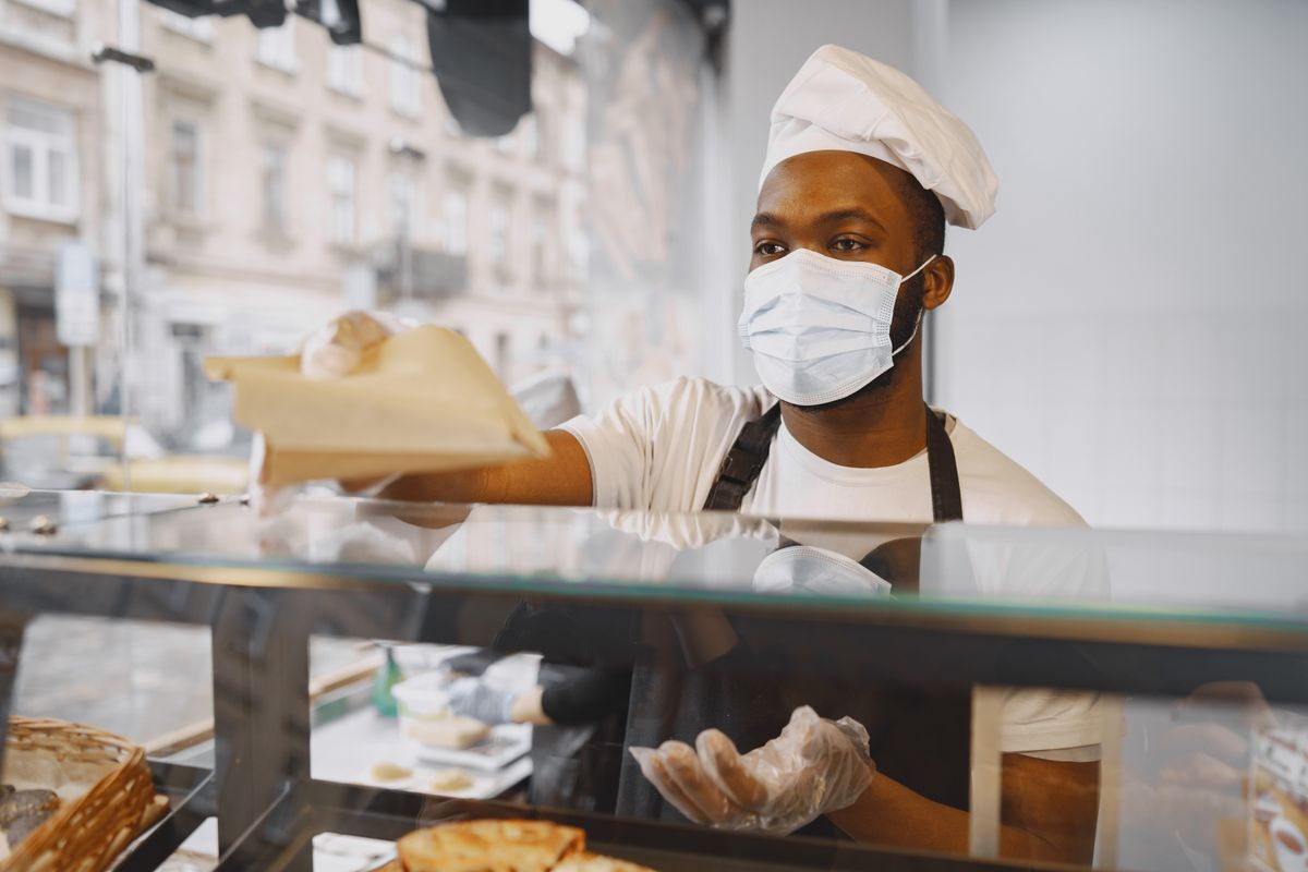 8 Jobs That Will Drain You, Age You, and Still Replace You Anyway 4 A baker wearing a face mask serves fresh bread to a customer in a modern bakery.