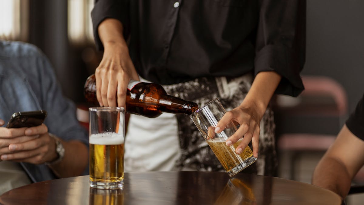 A bartender pours beer from a bottle into a glass at a bar, capturing a moment of social leisure.