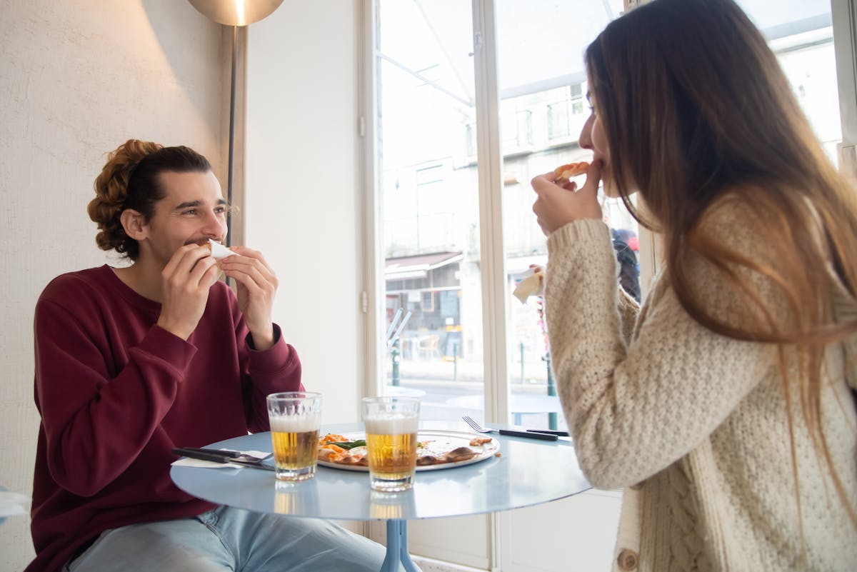 A cheerful couple sharing pizza and drinks in a cozy indoor setting.
