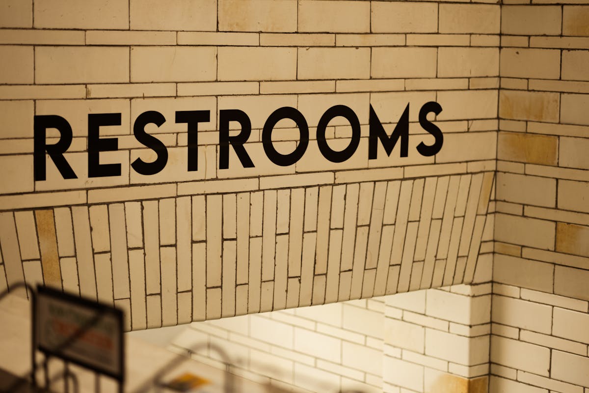 A clear restroom sign displayed on a tiled wall, indoors.