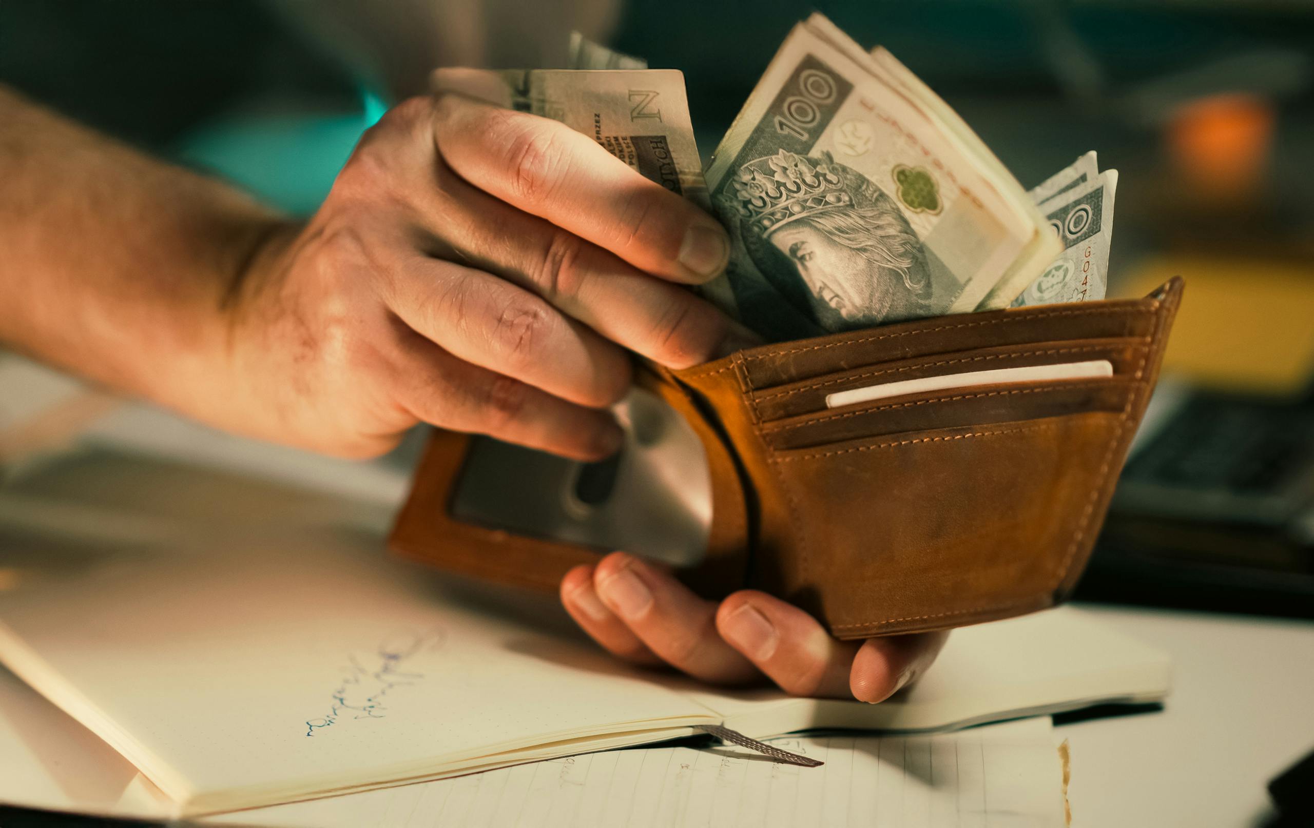 11 Harsh Truths About Marriage After 30 Years That Couples Quietly Learn 5 A close-up of hands holding a wallet filled with Polish banknotes on a desk.