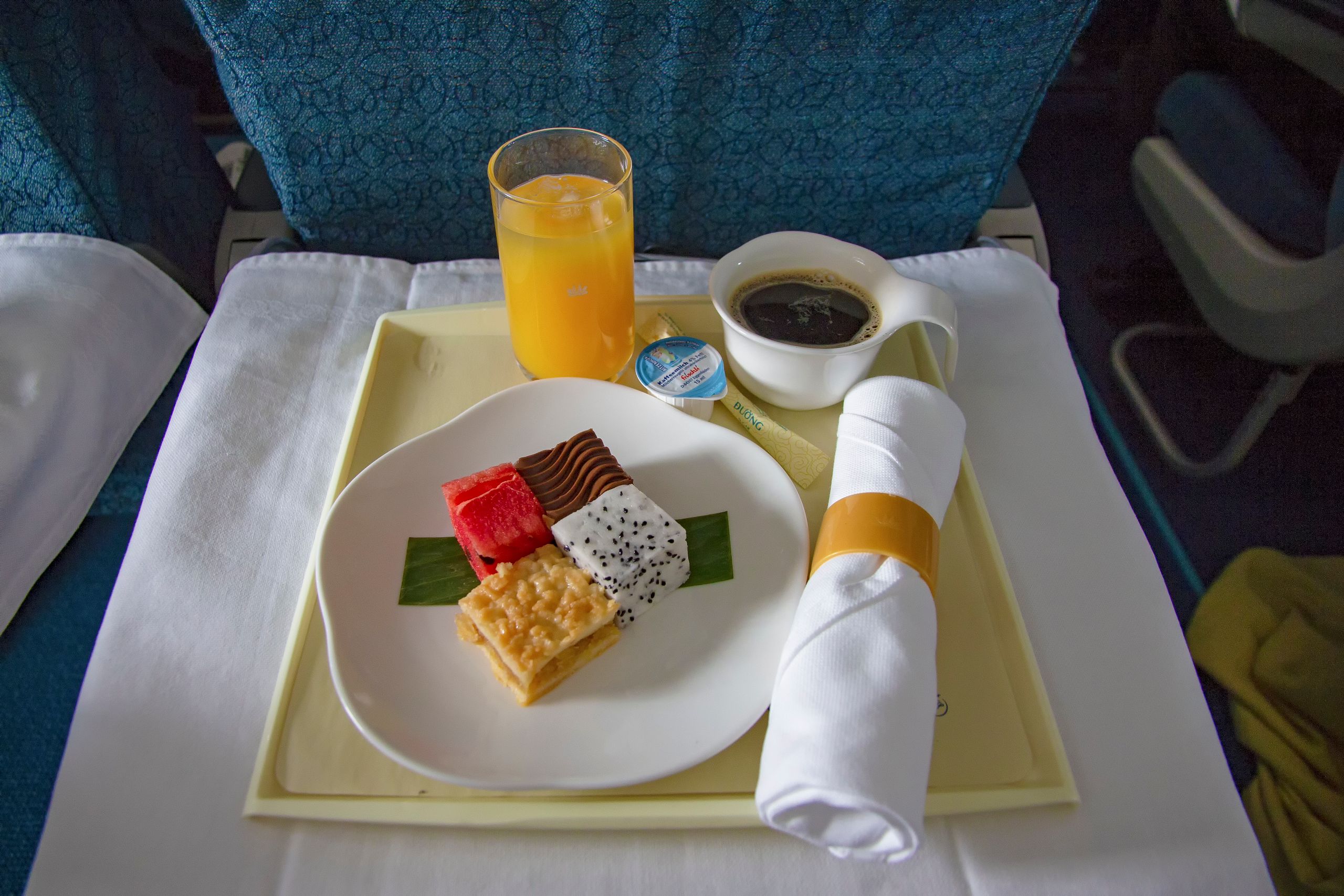 A colorful in-flight meal tray featuring desserts, orange juice, and coffee.