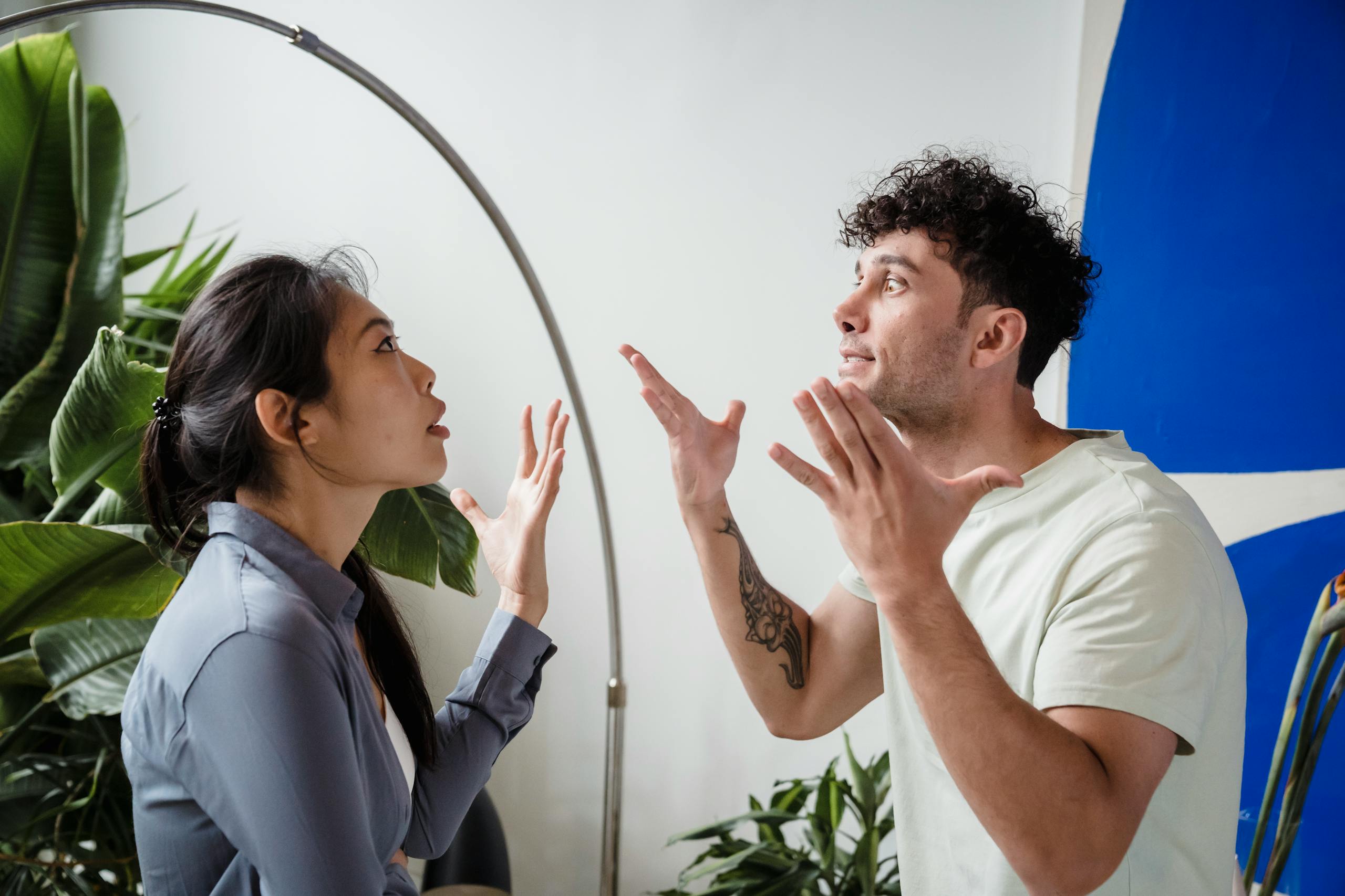 8 Warning Signs Your Relationship Is Quietly Falling Apart 1 A couple argues indoors amidst greenery, showcasing emotions and interpersonal conflict.