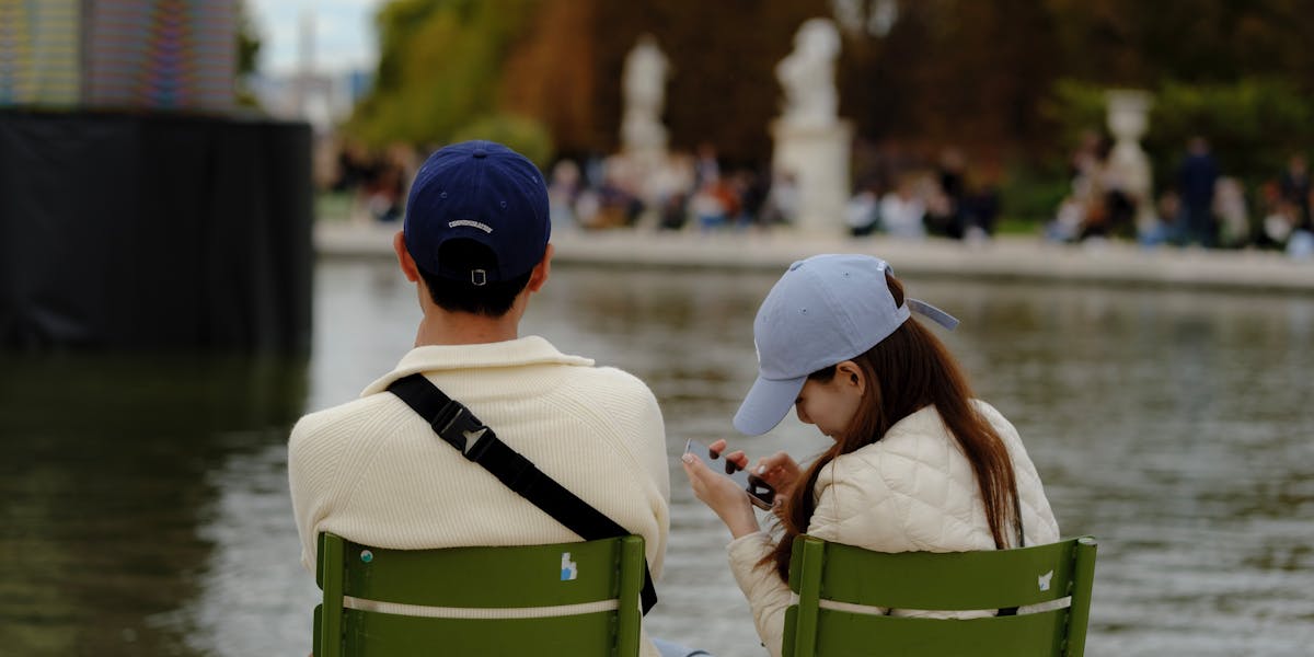 A couple seated by a fountain, engrossed in a smartphone outdoors.