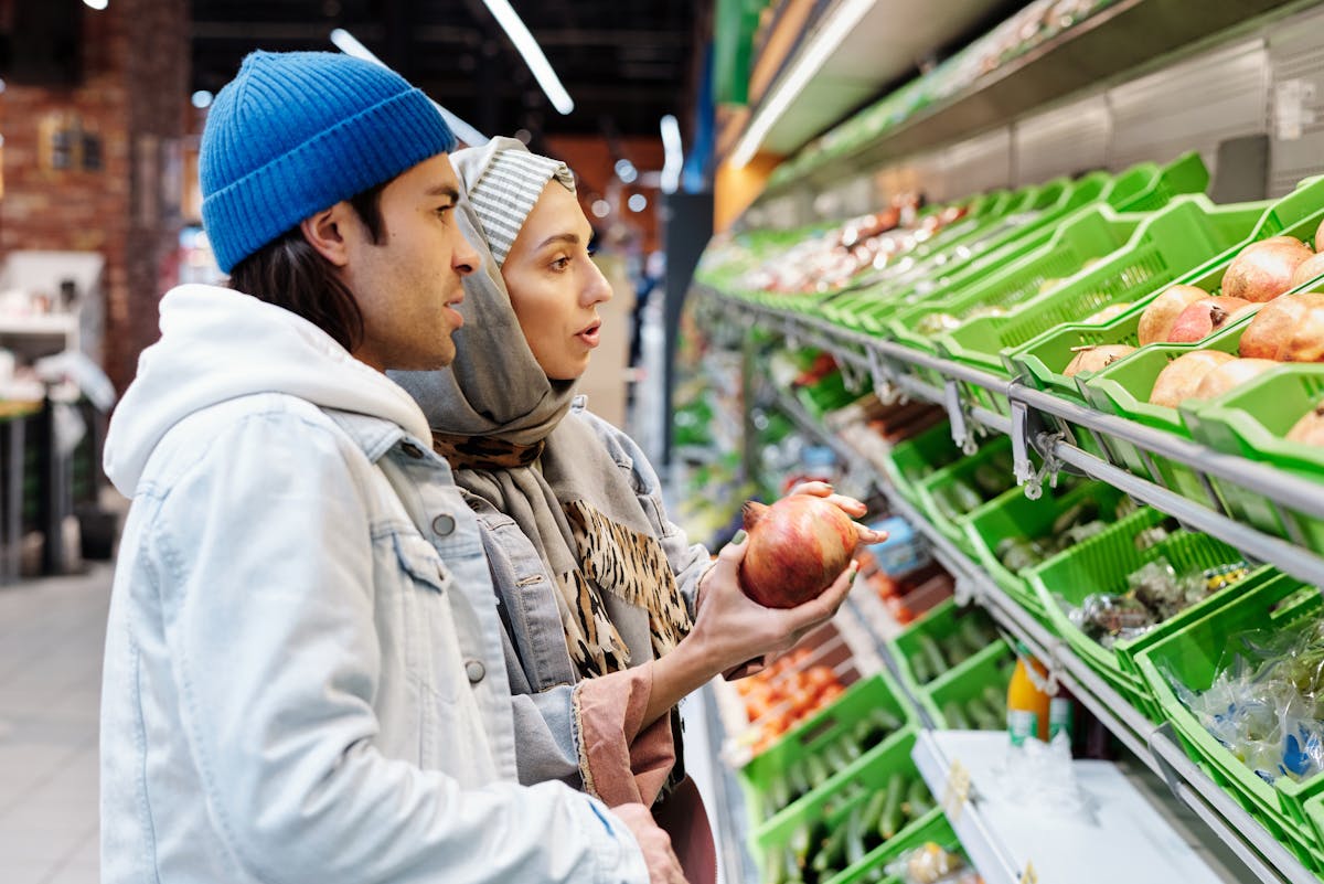 A couple selecting pomegranates in a grocery store aisle filled with fresh produce.