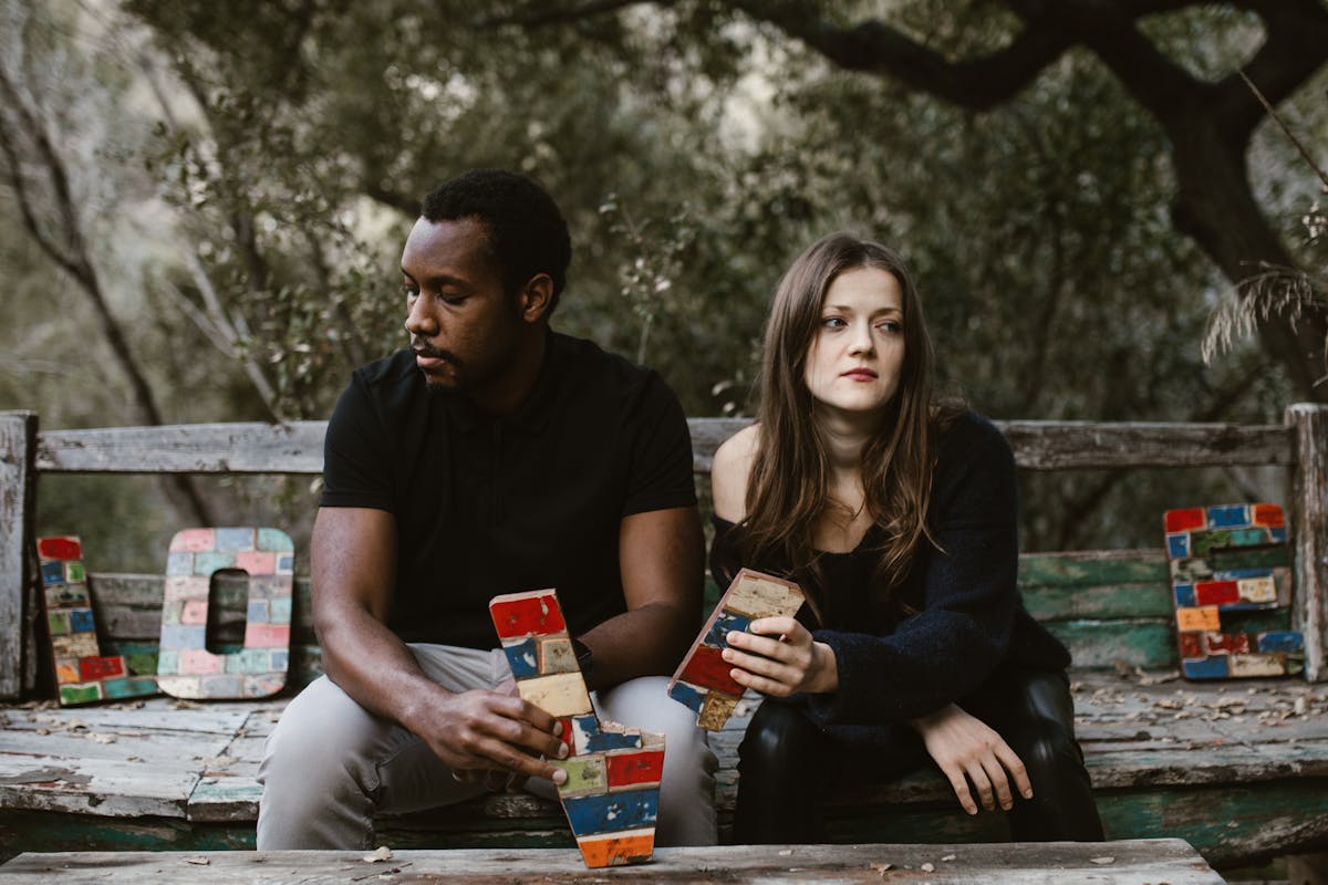 10 Things Men Find Unattractive in Women 5 A couple sits in tension on a bench surrounded by nature, holding colorful blocks spelling 'Love'.