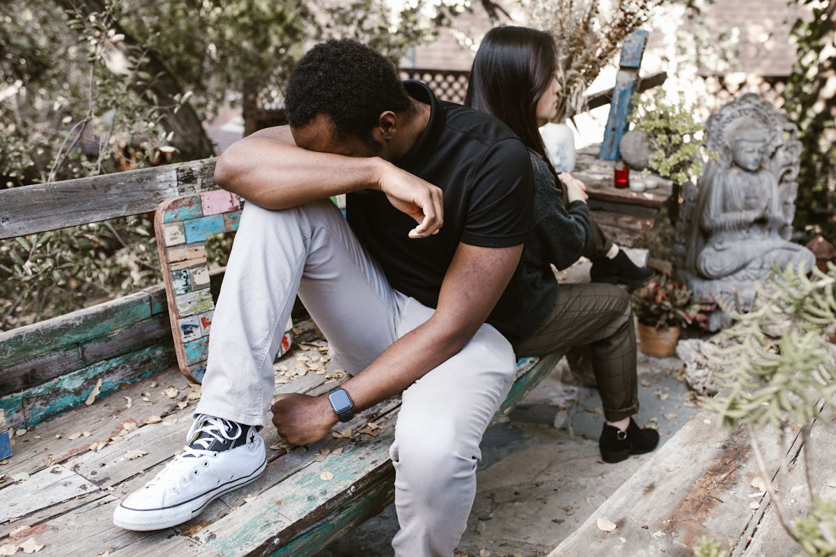 13 Signs a Man is Unhappy in Marriage 2 A couple sitting back to back in a garden, expressing sadness and tension.