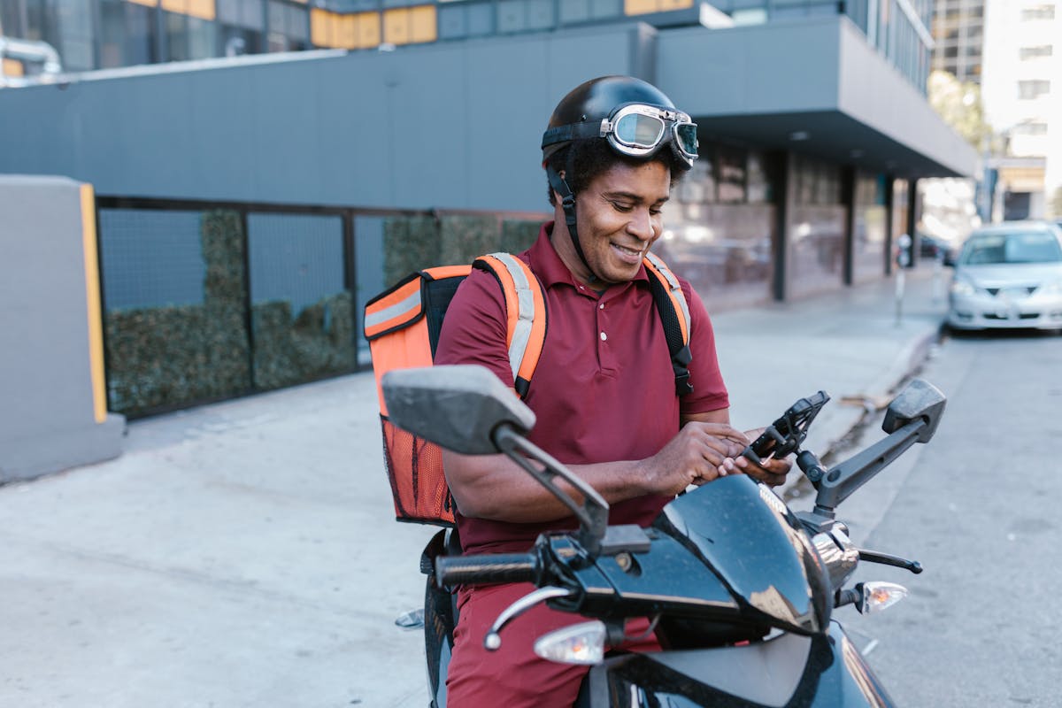 A delivery rider checks his smartphone while sitting on a motorcycle in the city.