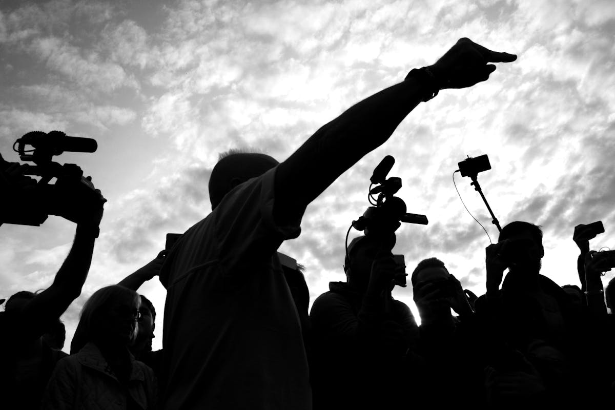 7 Shocking Election Results in US History That Changed America Forever 3 A dramatic silhouette of a media crew with cameras capturing a pointing individual against a cloudy sky.