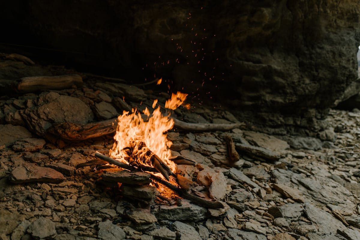 A glowing campfire surrounded by rocky terrain emits warmth and light outdoors.