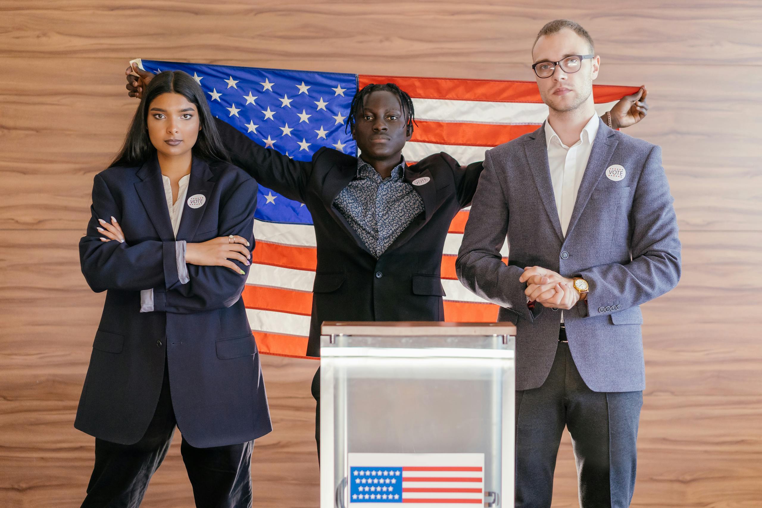 7 Ways America’s Immigration Fight Is Tearing Ordinary Communities Apart 4 A group of diverse individuals standing confidently in front of an American flag at an election podium.