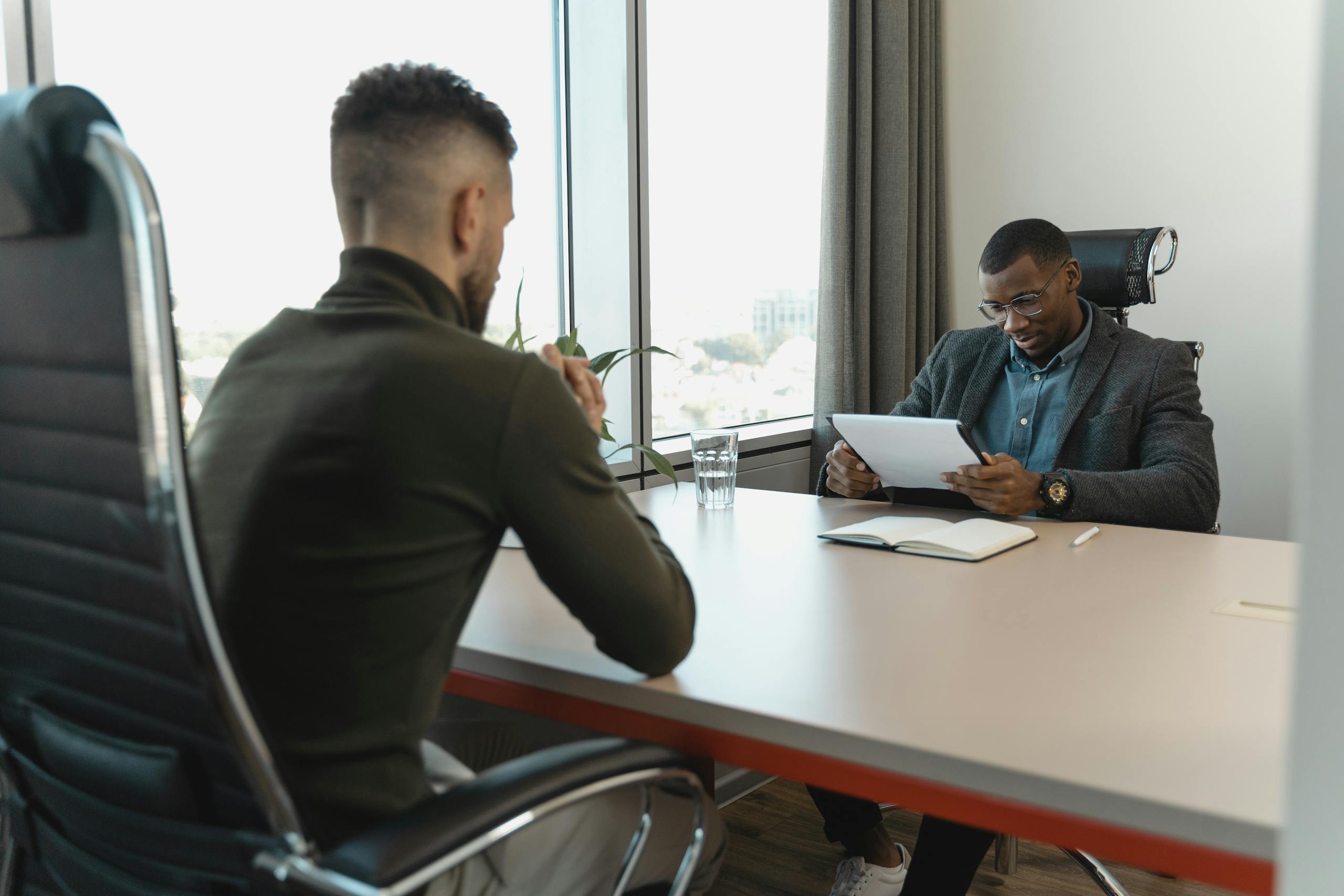 7 Reasons Americans Don’t Believe the Economy Is Fine Anymore 3 A job interview taking place in a modern office setting between two professional men.