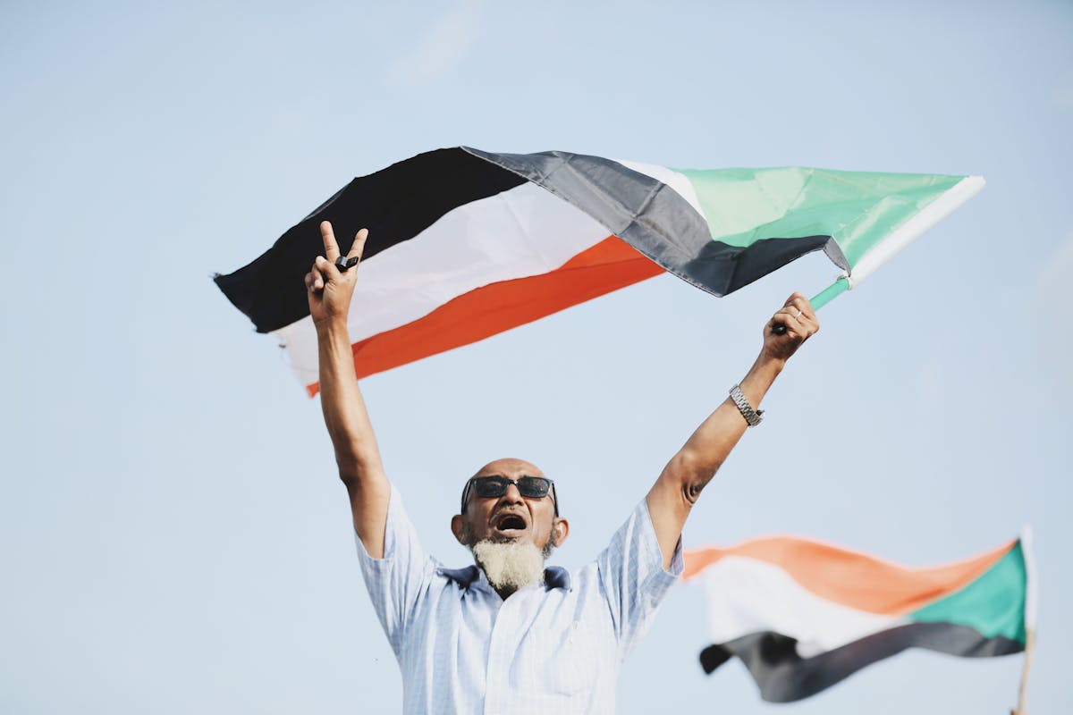 8 World’s Most Corrupt Nations Right Now 4 A joyful man holds the Sudanese flag, celebrating outdoors with a victory sign.