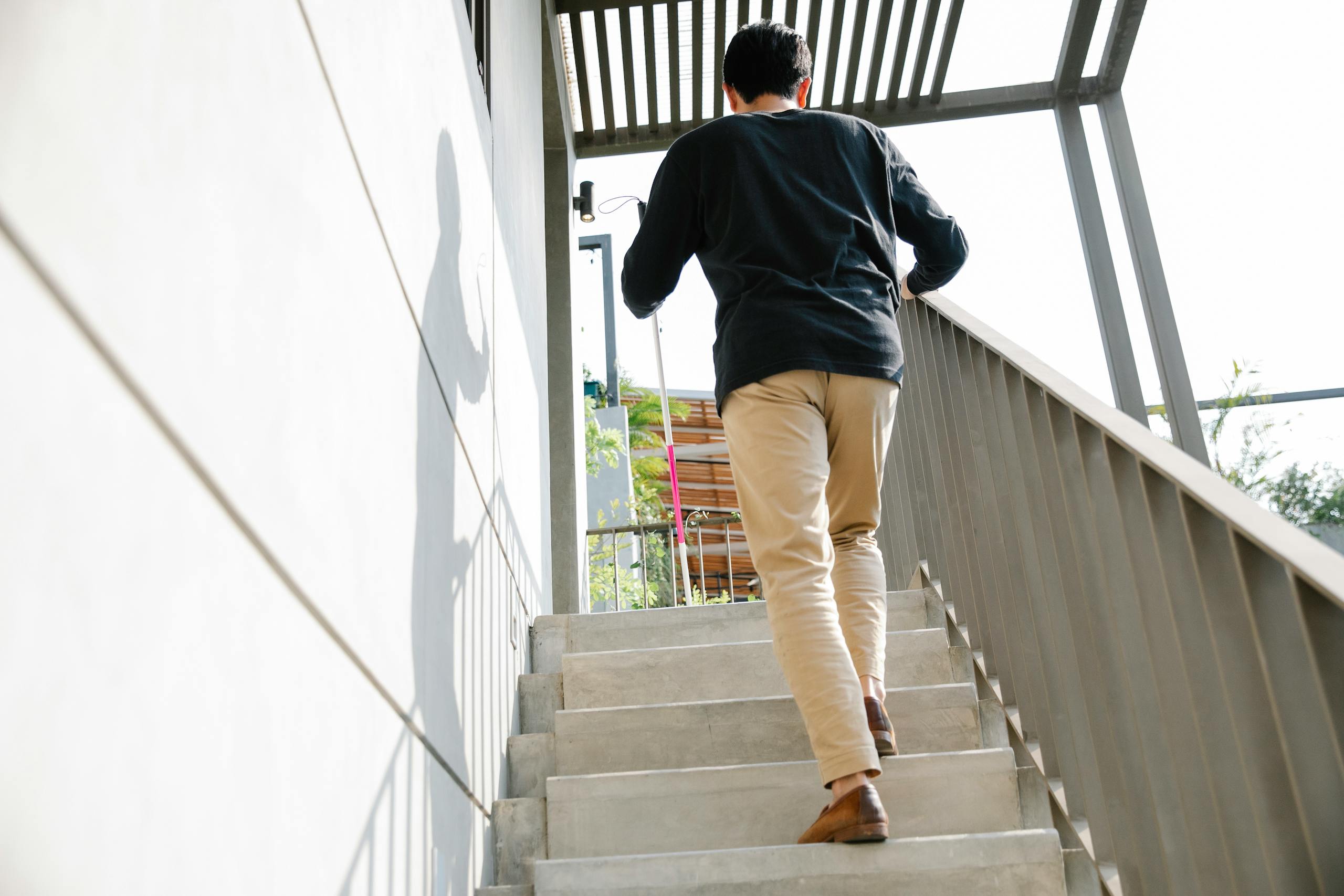 A man is seen walking up an outdoor staircase on a sunny day, casting a shadow on the wall.