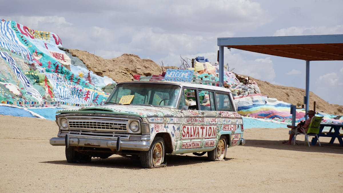 12 Dangerous Places in the U.S. We Wouldn’t Wish on Our Worst Enemy 5 A painted vintage car at Salvation Mountain in Slab City, showcasing vibrant art and desert background.