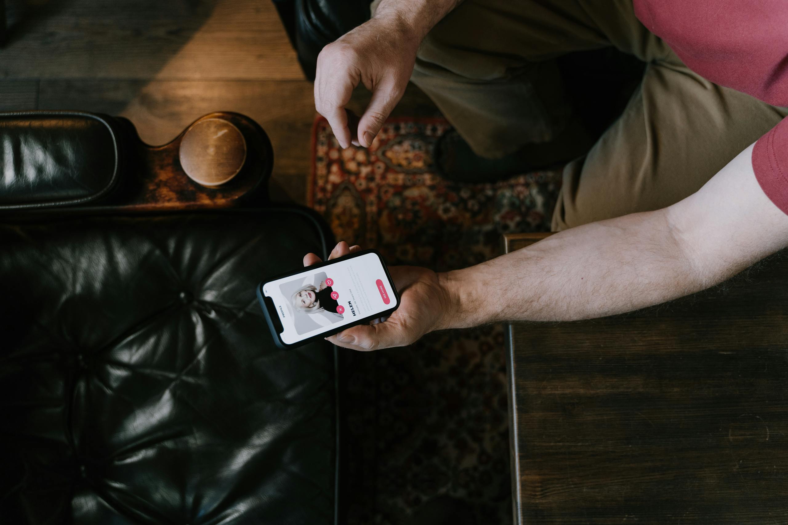 8 Brutal Dating Truths People Ignore 1 A person holding a smartphone with a dating app displayed while sitting on a leather chair.